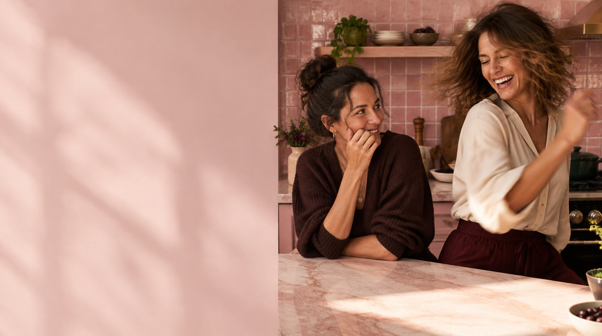 Two women sharing a joyful moment in a pink kitchen.
